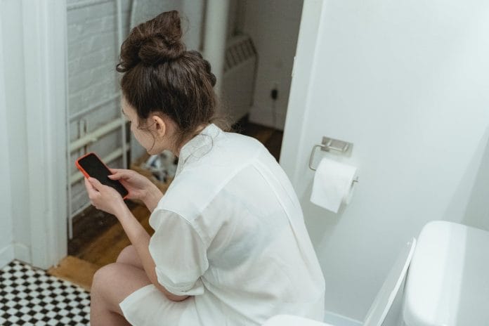 a woman using her cellphone while in the toilet